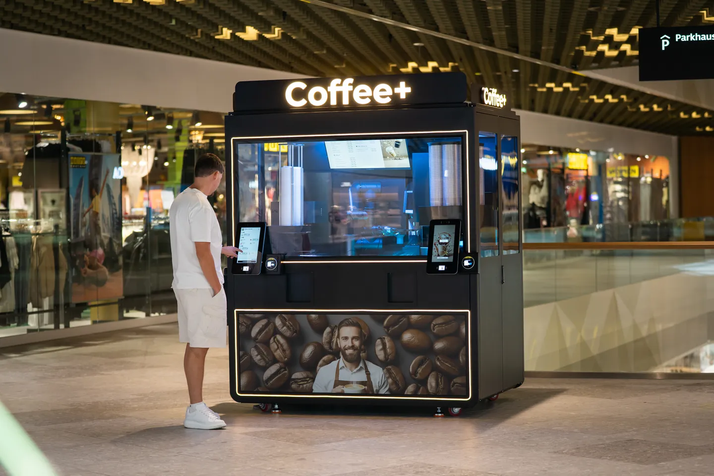 Ein Gast bestellt am Coffee+ Kiosk im Einkaufszentrum. Die komplette Anlage mit beiden Displays ist sichtbar.