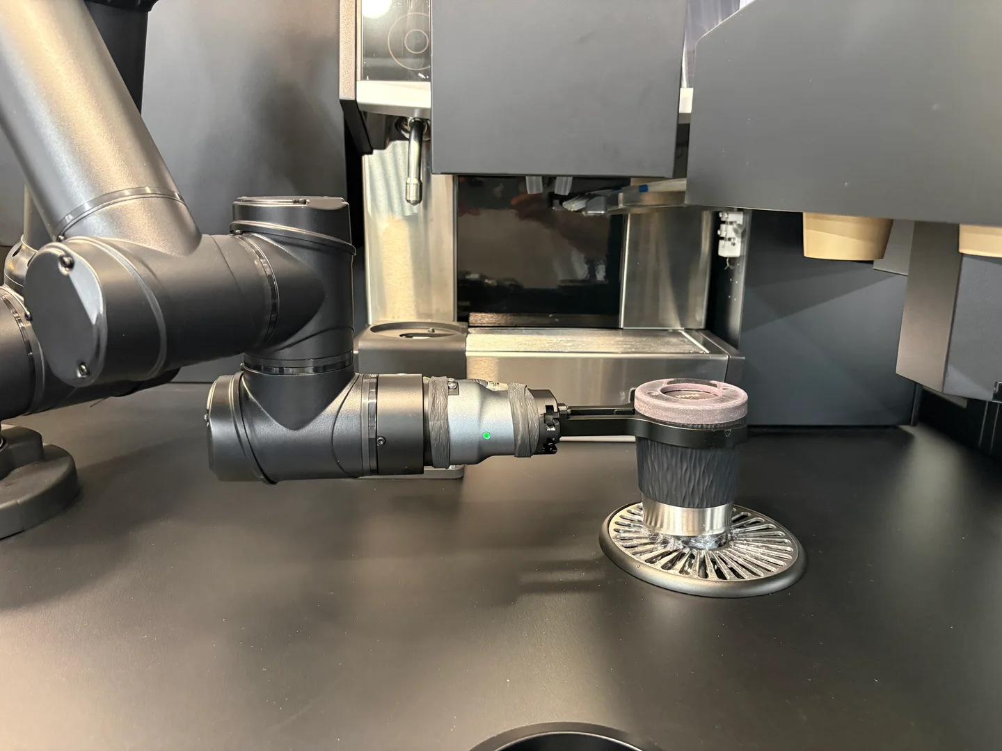 Blick ins Innere des Coffee+ Kiosks: Der Roboterarm hält ein Milchkännchen über der Spülstation.