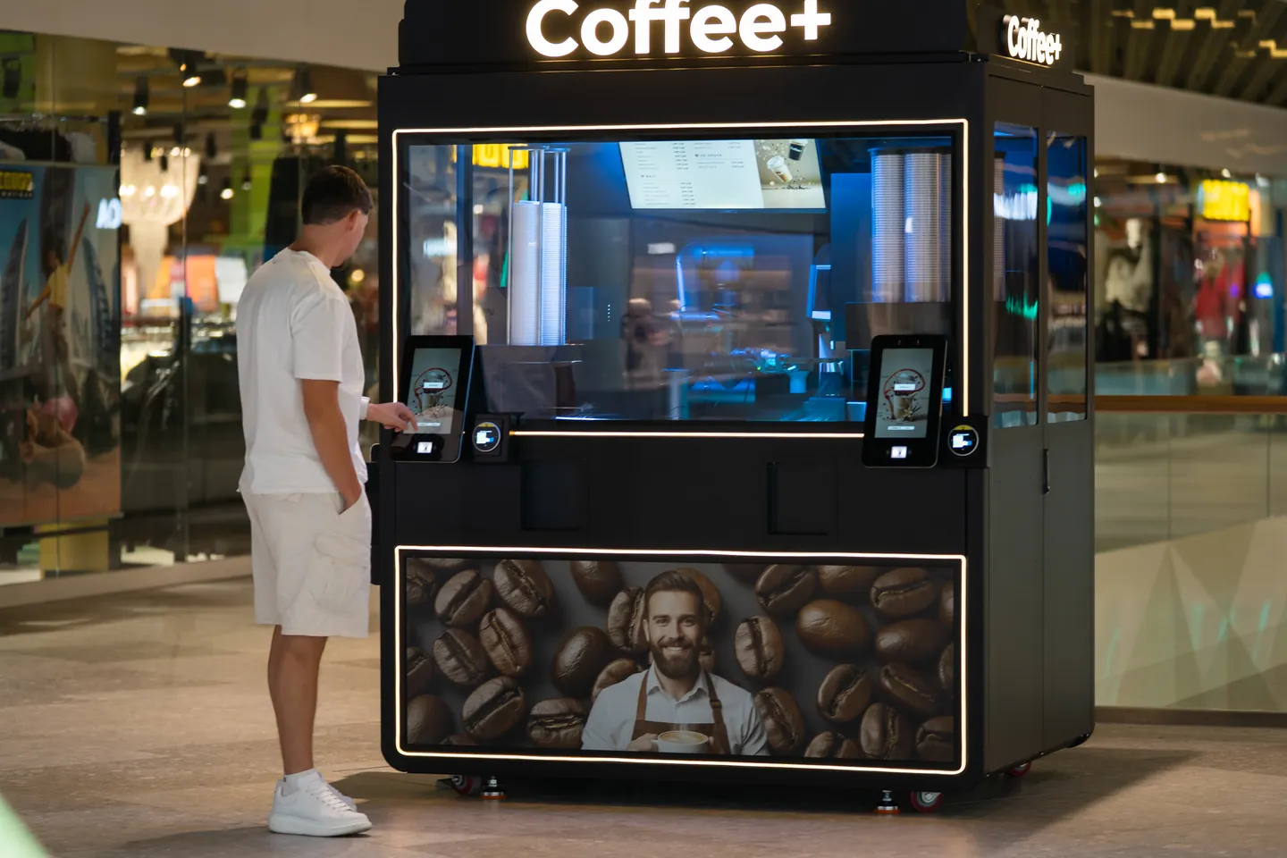 Die komplette Coffee+ Anlage mit sichtbarer Standfläche und einem Gast am linken Bestelldisplay.